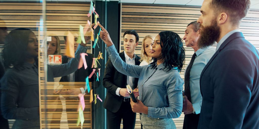 Group of people looking at post its on a glass wall