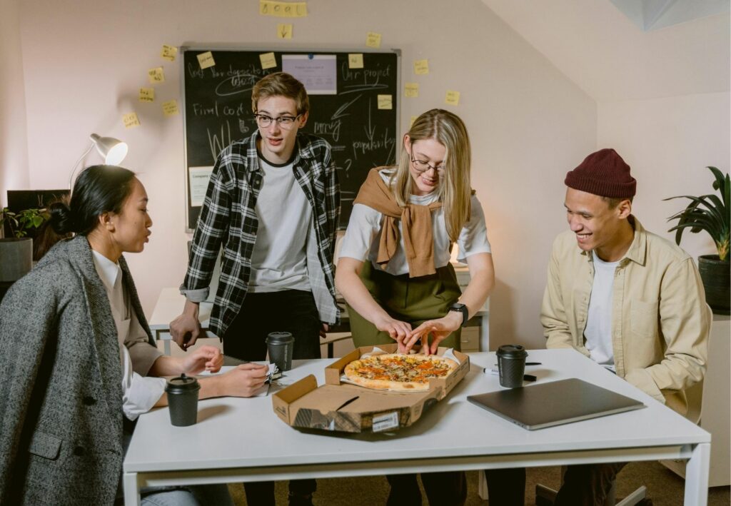 A diverse group of coworkers in a bright modern office, smiling and warmly interacting, symbolizing a workplace culture where everyone feels a strong sense of belonging.