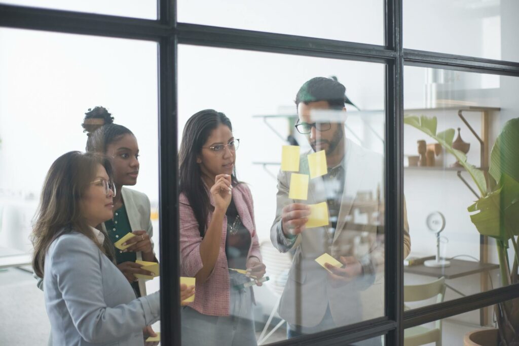 A group of four co-workers, three women and a man, working together in an office with post-it.