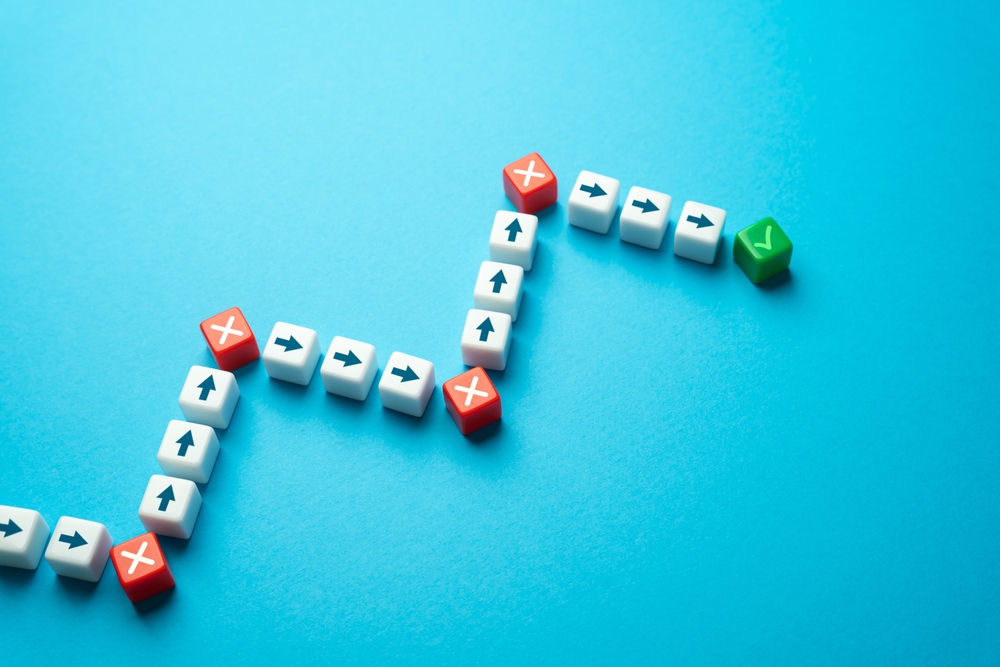 Illustrated path made of arrow-shaped blocks winding forward on a blue background, showing obstacles marked with Xs along the way and ending with a green checkmark, symbolizing progress through challenges.