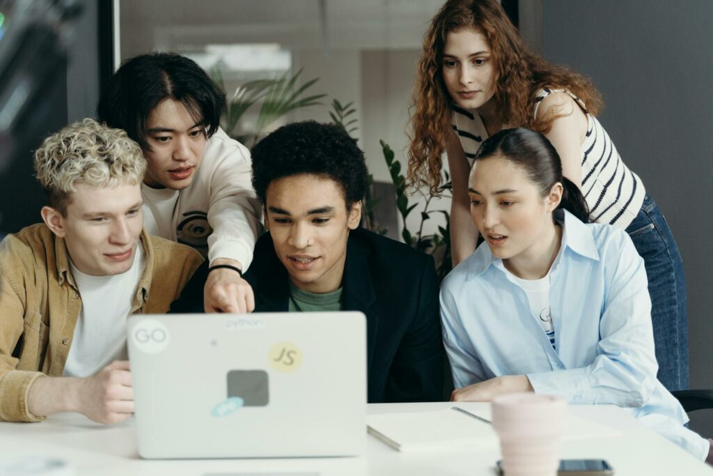 Five coworkers at a desk in an office working together around a laptop