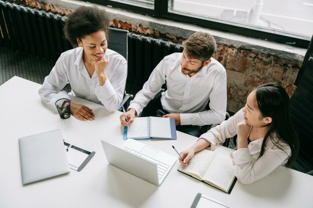 Picture of a group of three co-workers, one man and two women, around a white desk taken from above.