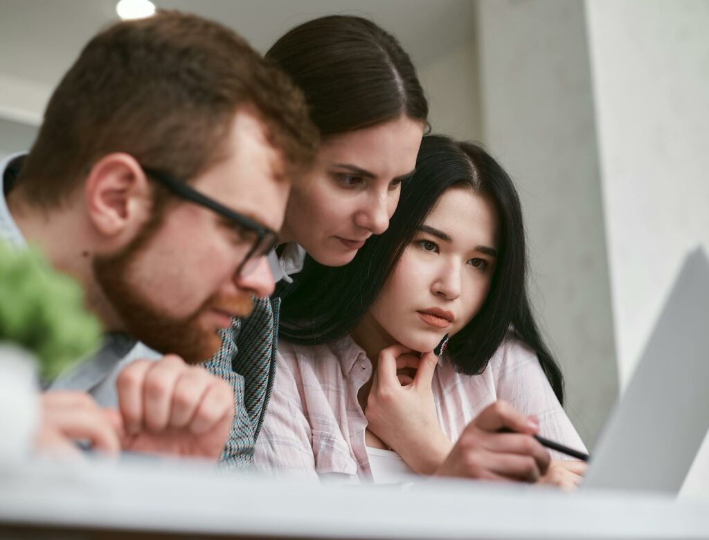 Three coworkers, one man and two women, leaning into a computer, working together.