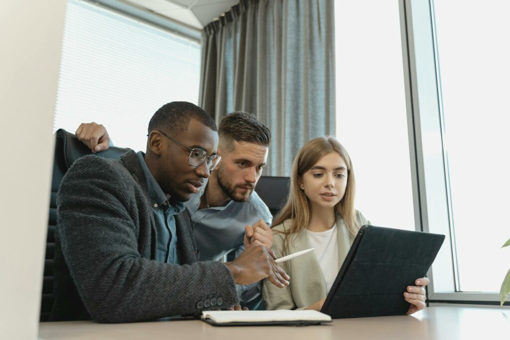 Three coworkers around a desk working and looking at a tablet device.